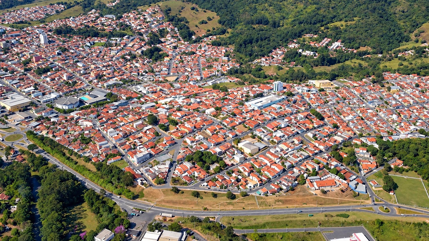 Imagem aérea aprimorada digitalmente da área urbana de Extrema, cercada por morros verdes, baseada em foto de divulgação.